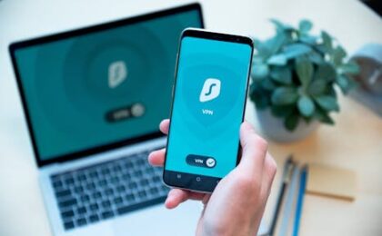 Close-up of a hand holding a smartphone with VPN app, laptop in the background, showcasing digital security.